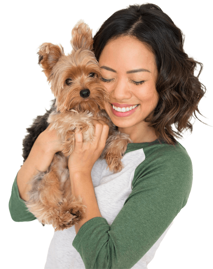 A woman with shoulder-length dark hair smiles while holding a small, fluffy dog in her arms against a plain white background.